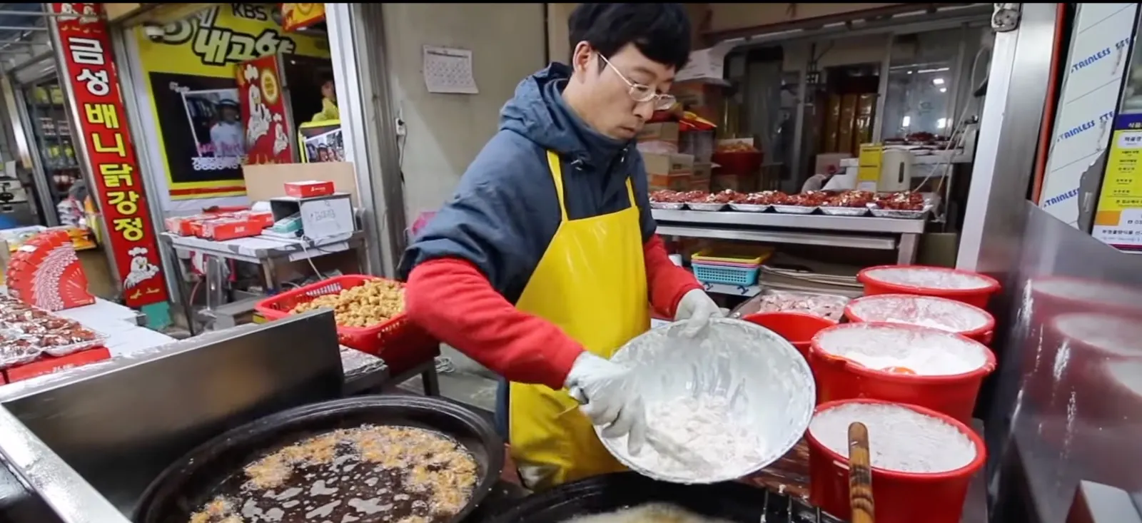 A Korean market vendor battering fried chicken over bubbling fryers